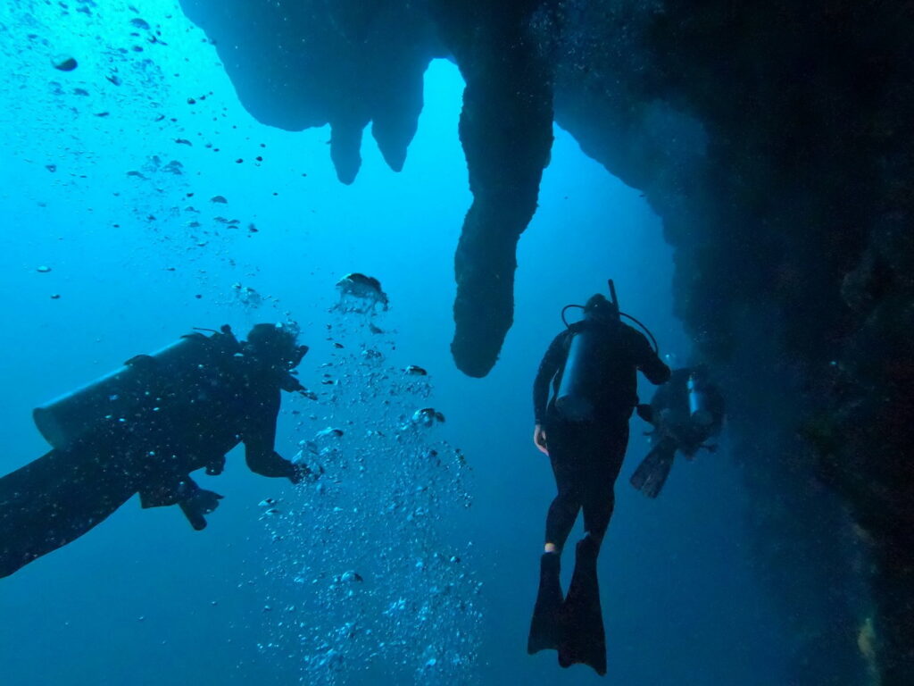 Scuba divers swimming beneath massive stalactites inside the Great Blue Hole, Lighthouse Reef Atoll, Belize