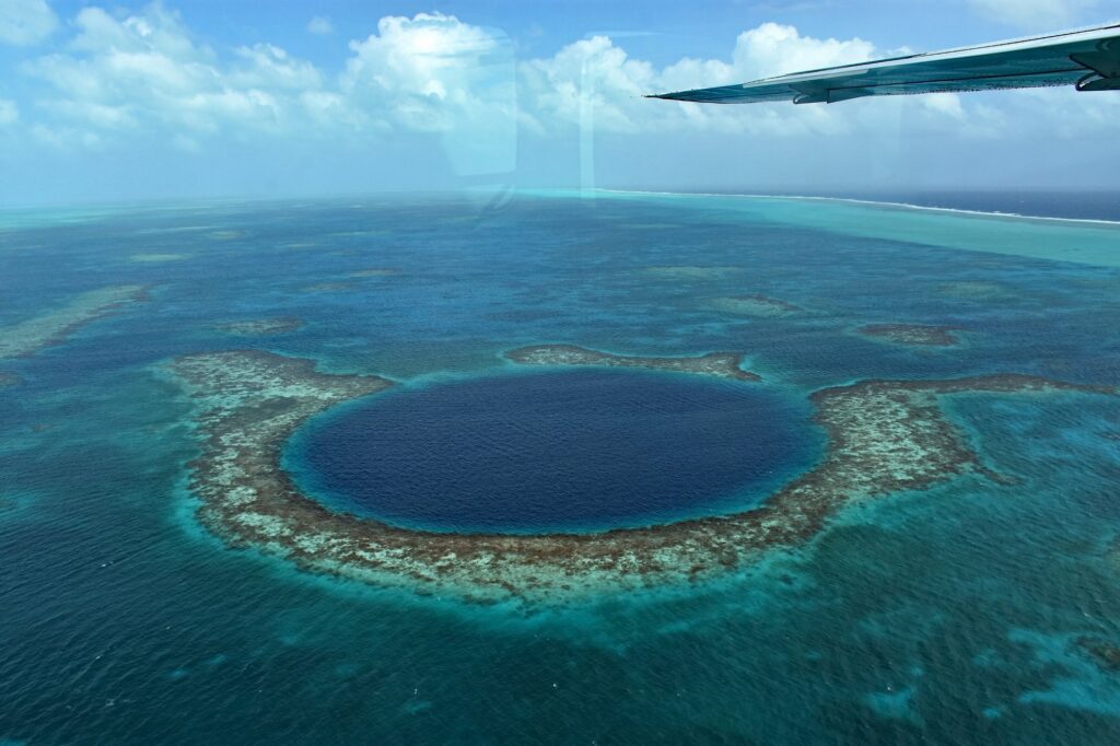 Aerial view of the Great Blue Hole in Belize from a scenic flight, showing the circular marine sinkhole surrounded by turquoise coral reef at Lighthouse Reef Atoll.