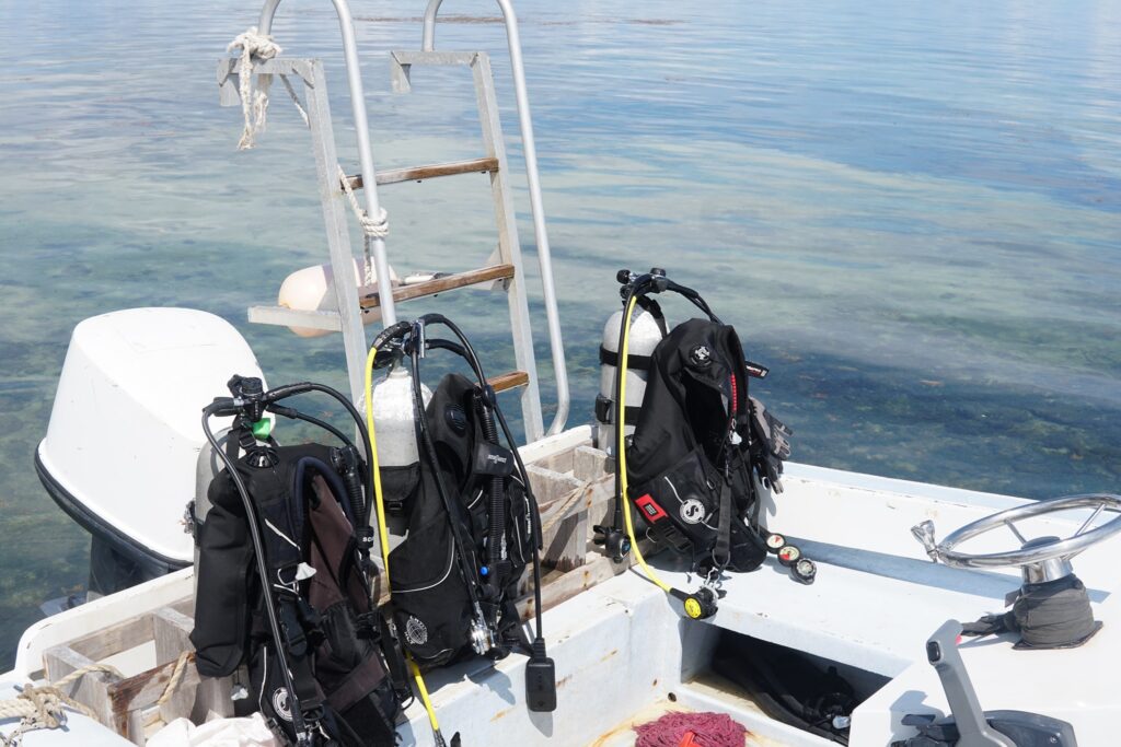 Close-up of the stern of a dive boat at Long Caye Belize with three scuba tanks and gear ready for a dive to the Great Blue Hole, calm clear Caribbean water in the background.