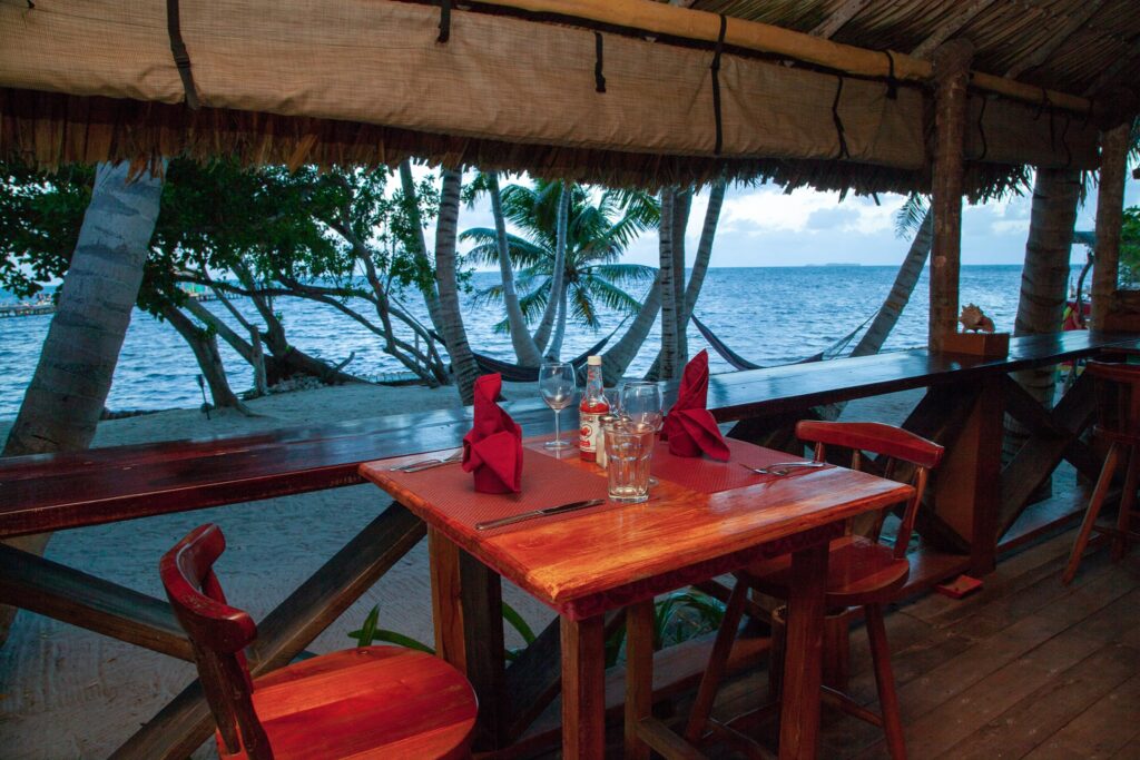Beachfront dining table setup at Itza Resort overlooking the Caribbean Sea on Lighthouse Reef Atoll Belize with palm trees and ocean view